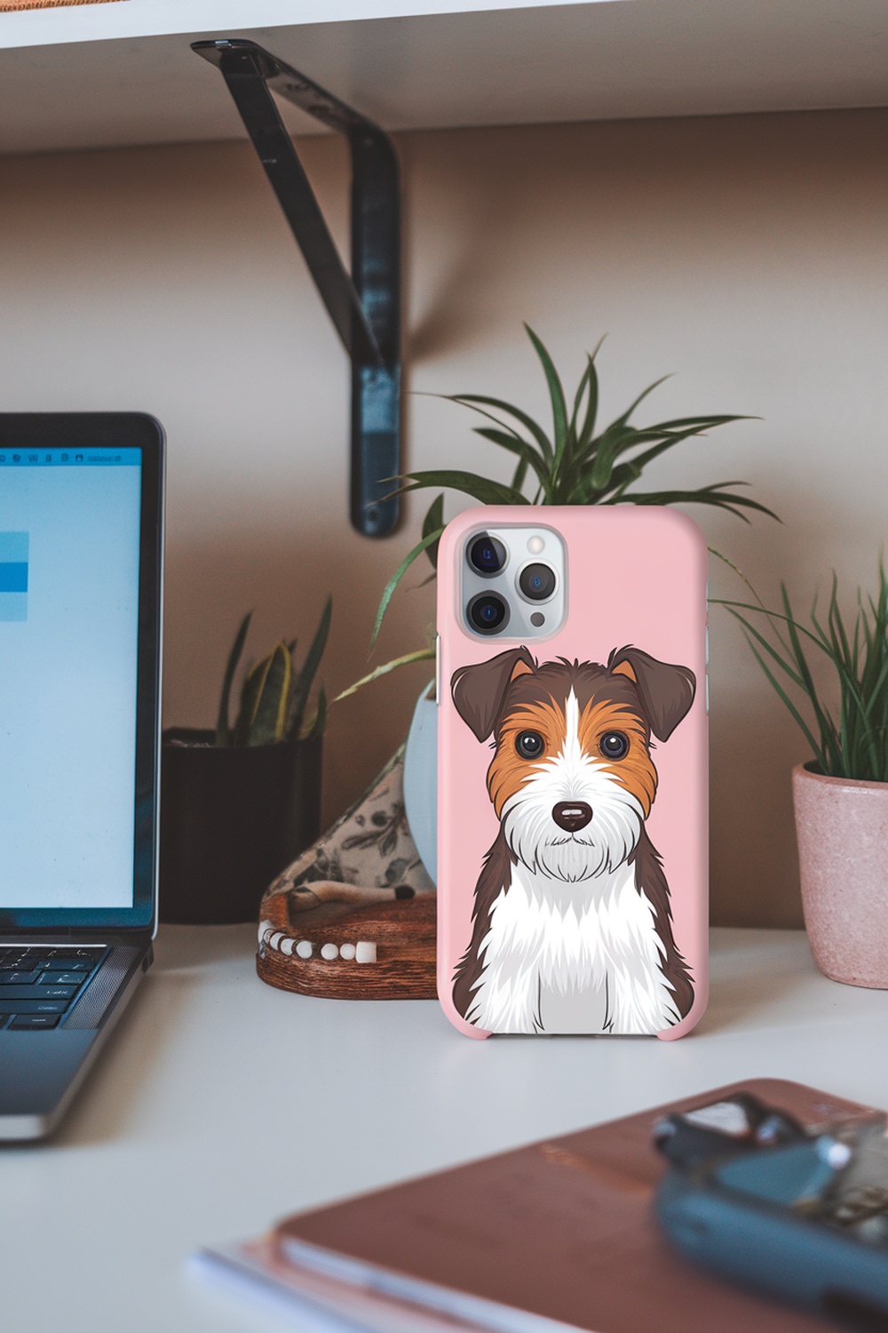 A phone case with a Terrier illustration on a desk with plants and a laptop.