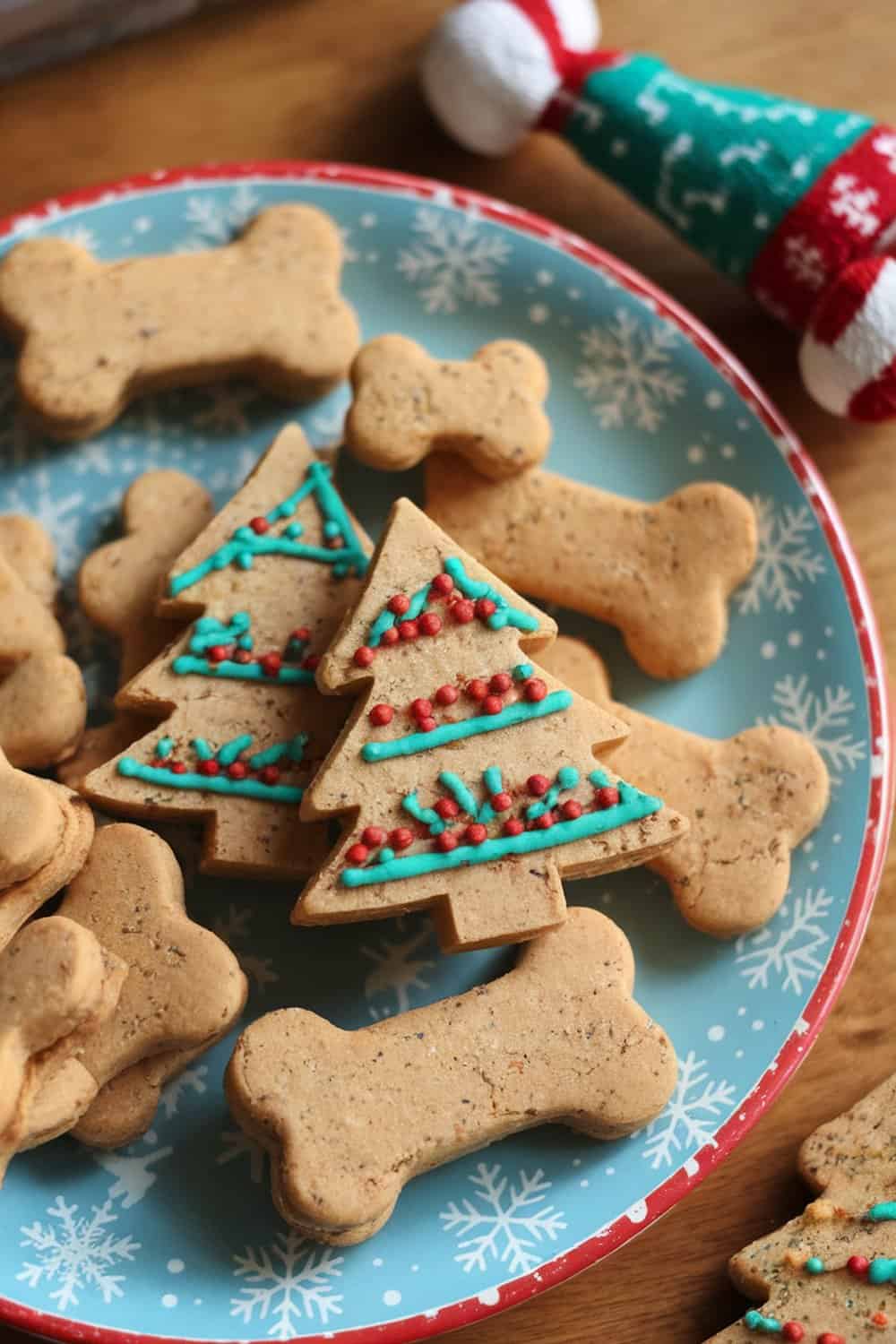A plate of homemade dog treats shaped like Christmas trees and bones, decorated with colorful icing.