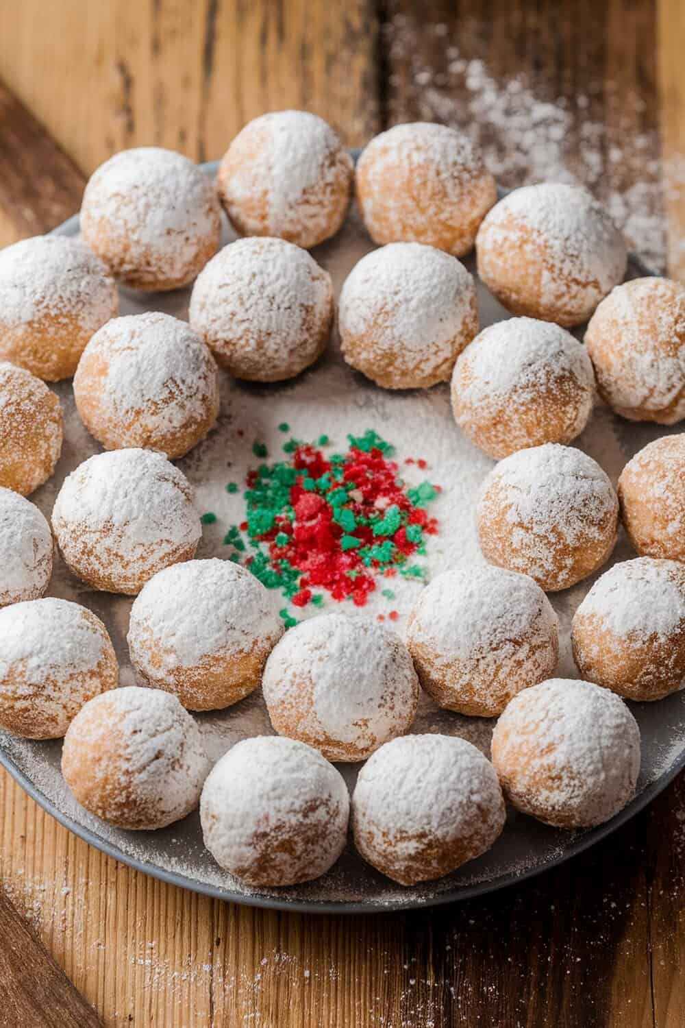 A plate of peanut butter snowball treats dusted with powdered sugar and colorful sprinkles.