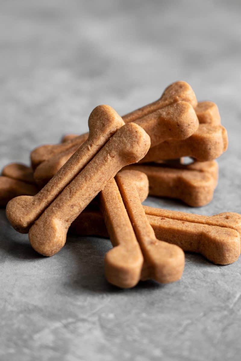 Dog biscuits in the shape of bones, arranged on a light gray textured surface. 